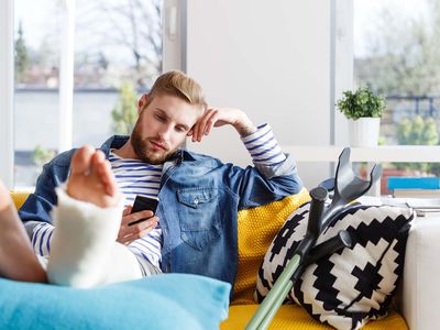 Young man with broken leg using smart phone at home