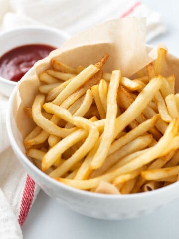 Air fryer shoestring fries in white bowl with a side of ketchup.