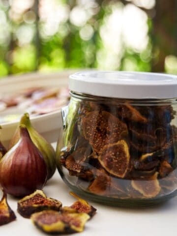 Dried figs in jar on table beside fresh figs and dried fig pieces.