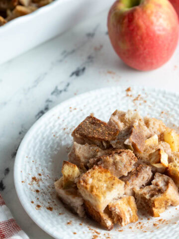 A plate with apple bread pudding topped with cinnamon.