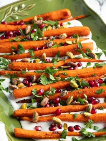 Roasted carrots on top of a cream sauce and topped with parsley, pomegranate seeds, and pistachios.