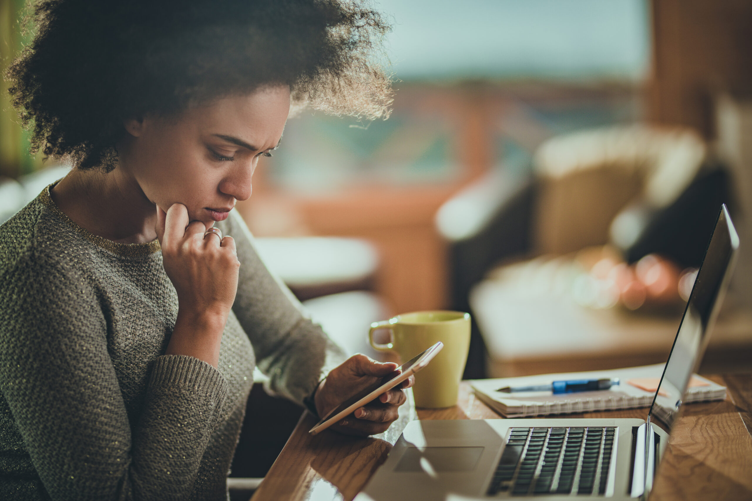 Young black woman reading a problematic text message on her mobile phone while working at home.