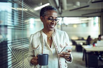 A woman standing in an office smiling at her smartphone