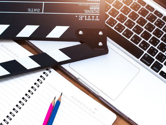 MacBook keyboard with a film slate resting upon it and a two pencils and a pad close by.