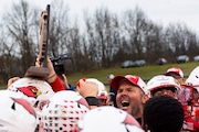 Millington’s head coach Jason Germain holds up a trophy while his team gathers around to celebrate their win during a high school football game, Saturday, Nov. 16, 2024, at Millington High School, 8780 Dean Drive, Millington. Millington won the game, 28-0. 