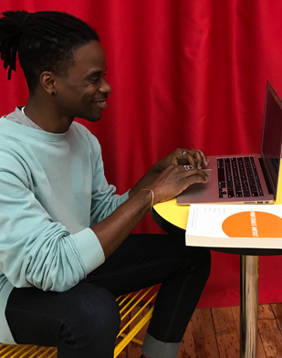 Image: A man smiles as he sits in front of his laptop computer.