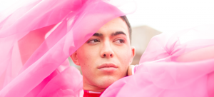 A young man is dressed in pink in a garment of his own design that relates to a dress he wore in the previous image at Camp I Am ten years prior. Today he is a fashion design student.