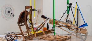 A group of ordinary objects is precariously arranged over three pallets, suspended on the border of collapse. Throughout the exhibition, the objects, initially leaning against the gallery walls, are activated and moved to be part of the composition in fragile balance. On the walls, colorful outline drawings record the objects' displacement.