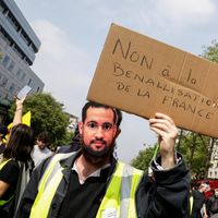 Manifestant gilet jaune portant un masque d'Alexandre Benalla et une pancarte "Non à la Benallisation de la France" lors des marches du 1er mai 2019 à Paris