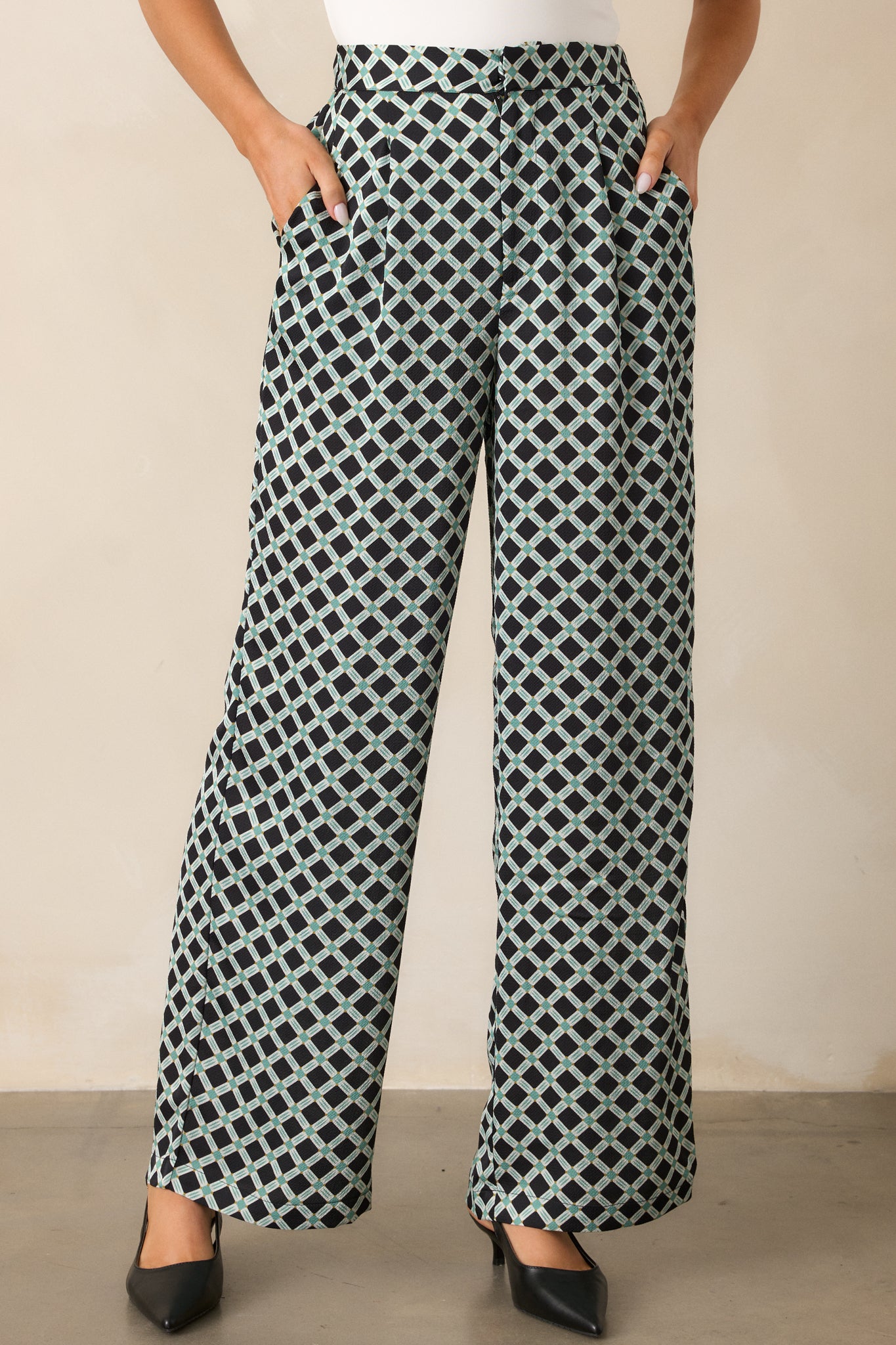 Cropped view focusing on the high waist design and the intricate green and white geometric print of the black pants.