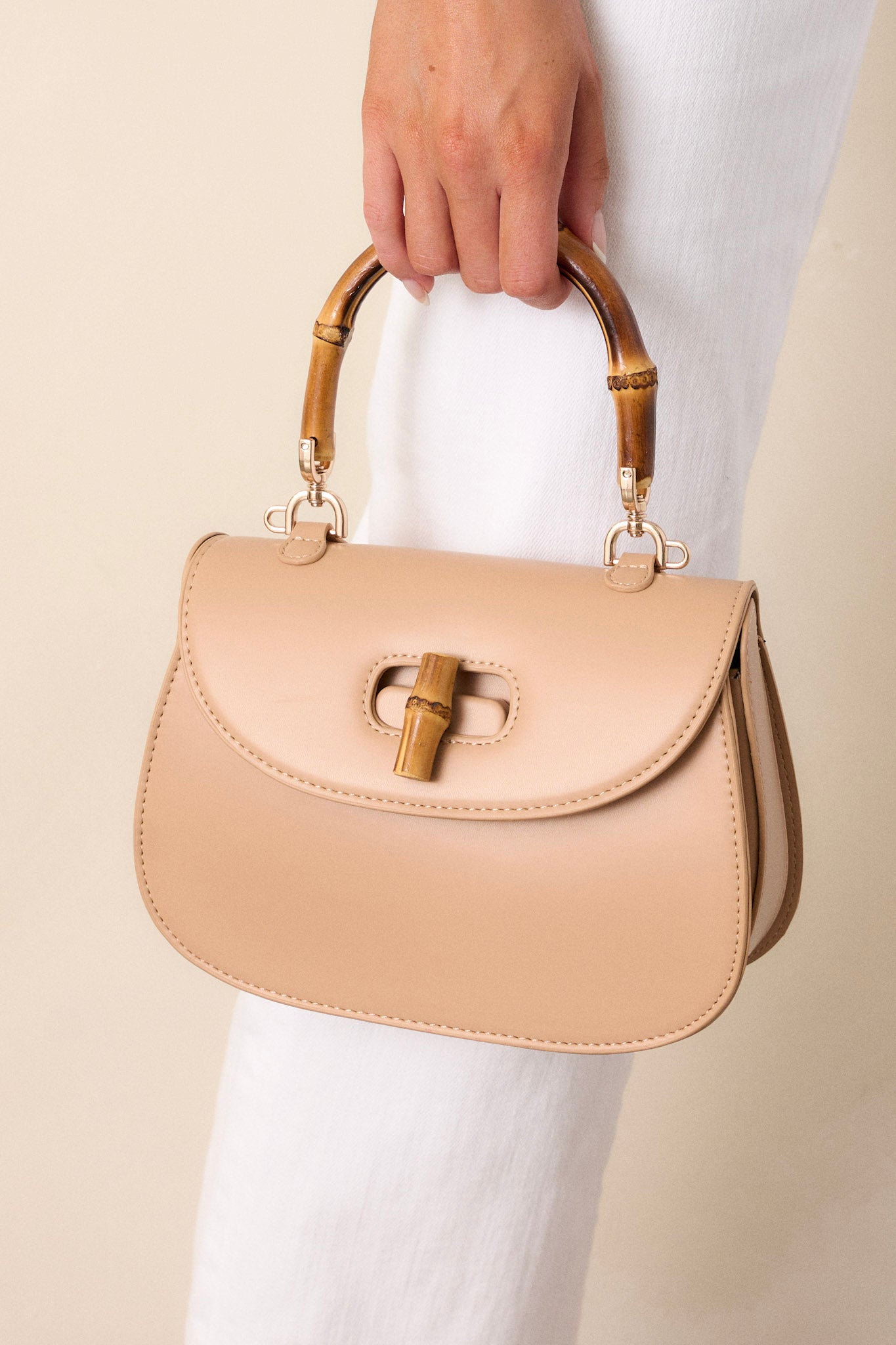 Close-up of this beige handbag that features a single flap design, a bamboo top handle, a bamboo twist lock closure, and a removable strap.