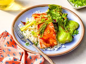 Plate of 5-ingredient sheet pan salmon with rice and bok choy at a table setting with glasses of wine, small platter with sliced green onions, and a blue and pink table napkin