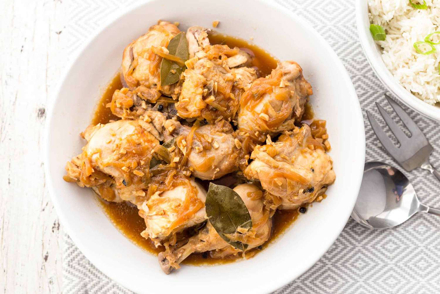 Bowl of Instant Pot Chicken Adobo Next to a Bowl of Rice Topped With Scallions and Utensils, All on a Placemat