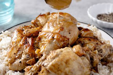 A platter of chicken adobo over rice and a serving spoon drizzling sauce over the chicken