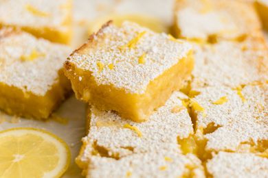 Lemon Bars Spread Out on a Parchment Surface and One Stacked Next to a Lemon Slice