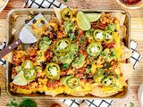 Baking Sheet of Vegan Nachos (Nachos Topped with Salsa, Queso, Pickled Jalpenos, and Two Lime Wedges) with a Serving Missing 