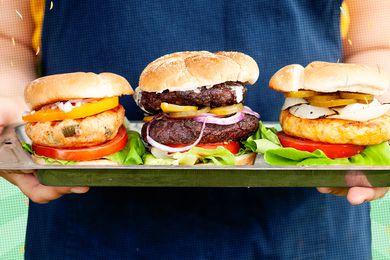 Person holding a tray of three burgers. 