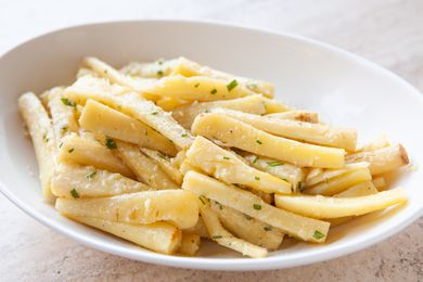 A white serving dish with roast parsnips inside.