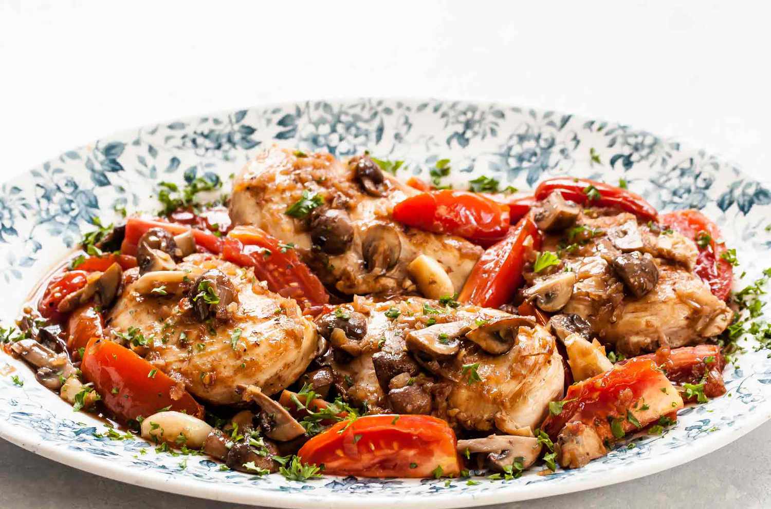 chicken, mushrooms, and tomatoes in a port sauce in a white bowl with flowers