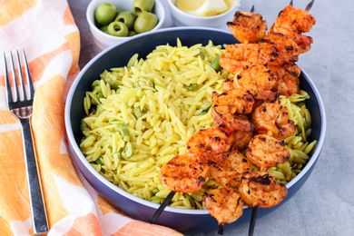 Harissa Grilled Shrimp with Orzo and Olives Next to Small Bowls with Olives, Lemon Wedges, and a Fork on a Cloth Napkin