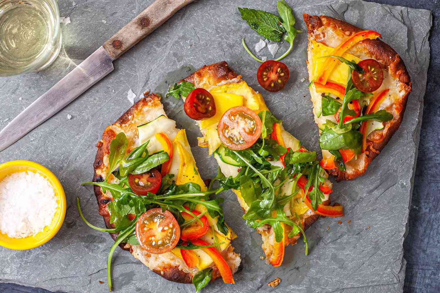 naan pizzas topped with summer vegetables on a gray slate