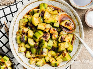 Chinese Cucumber Salad with Dark Vinegar and Chili Crisp Surrounded by a Small Bowl with Salt, Another with Sauce, and Another Bowl with Some Salad