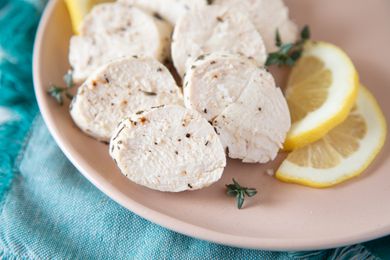 Sliced poached chicken on a plate with lemon slices.