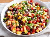 Stone fruit and vegetable salad in a serving bowl with a linen underneath.