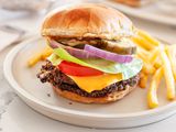 Black Bean Smash Burger on a Plate with French Fries, and in the Background, a Plate with More Burgers and a Tray with More Fries