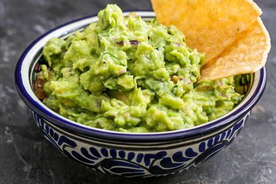 A bowl of guacamole with two tortilla chips i nit