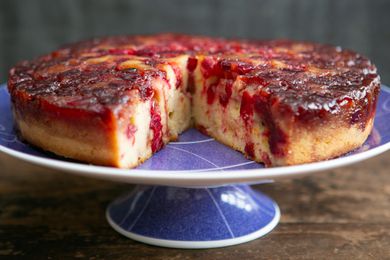 A cranberry upside-down cake on a platter with a slice cut out of it