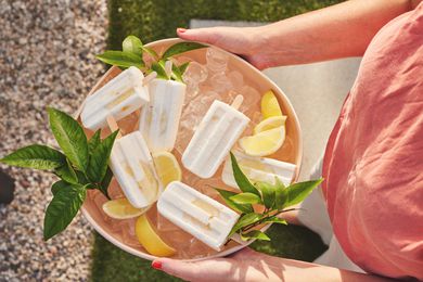 Someone Holding a Bowl of Limoncello Yogurt Pops on Ice Surrounded by Leaves and Lemons over Grass