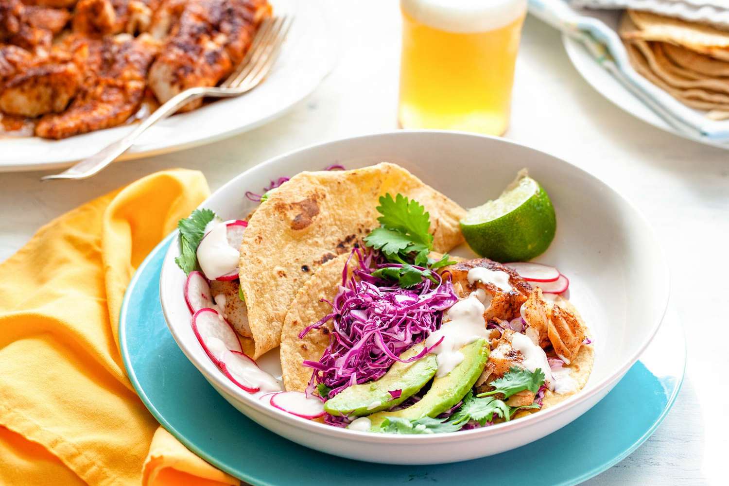 fish tacos in a white bowl served with a beer