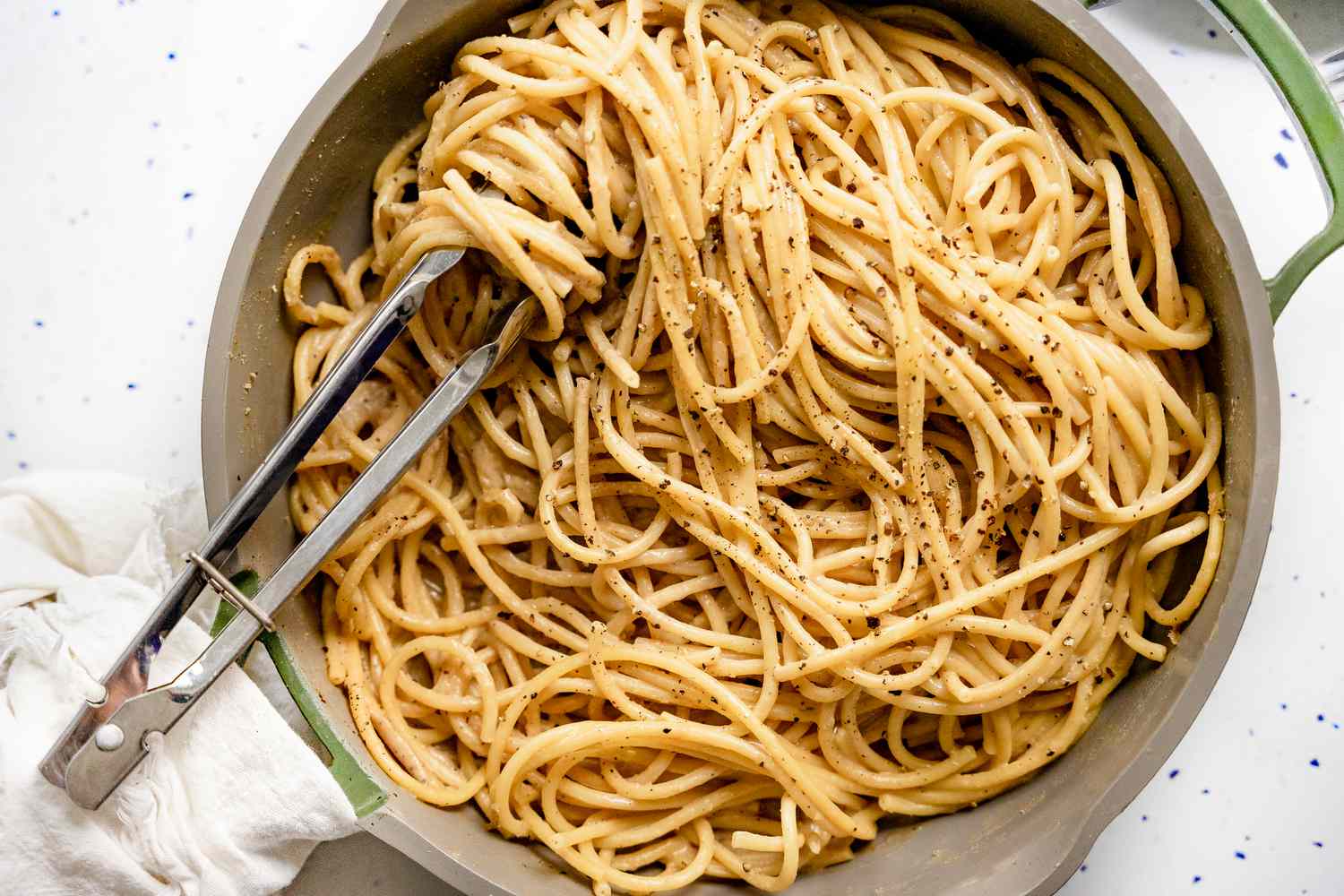 Pot of Vegan Cacio e Pepe with Some Noodles Wrapped around a Pair of Tongs