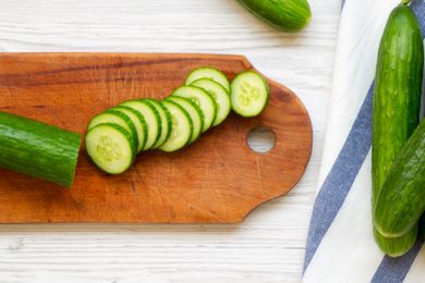 cucumbers sliced on a cutting board next to more (uncut) cucumbers on the counter