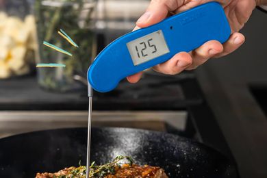 Thermapen thermometer measuring the temperature of steak cooking in a cast iron skillet