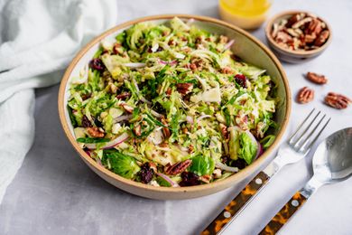 Brussel Sprout Cole Slaw in a Bowl Next to a Bowl of Dressing and Bowl of Pecans