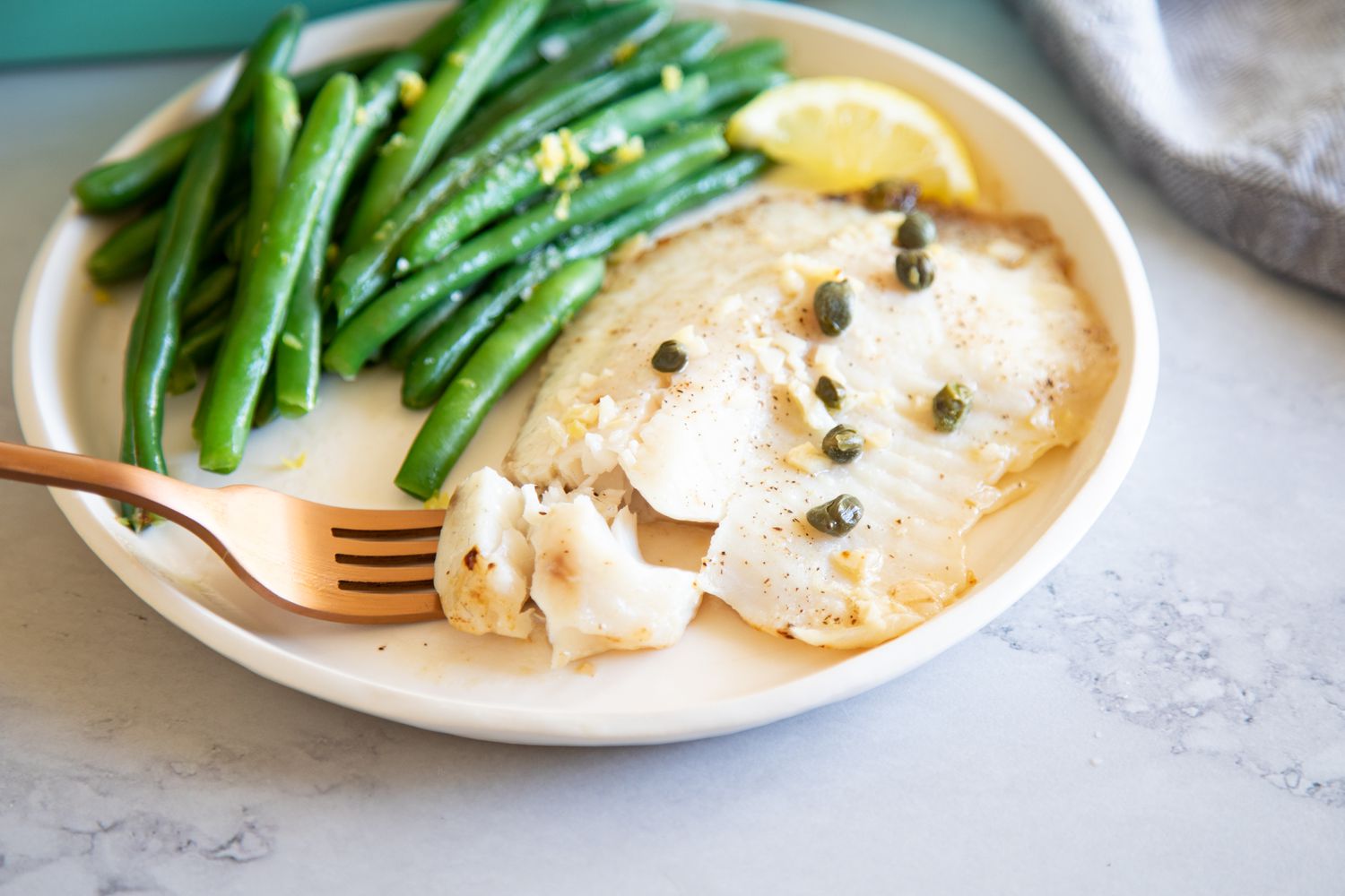 Lemon Butter Oven Baked Tilapia on a plate with a fork and green beans.