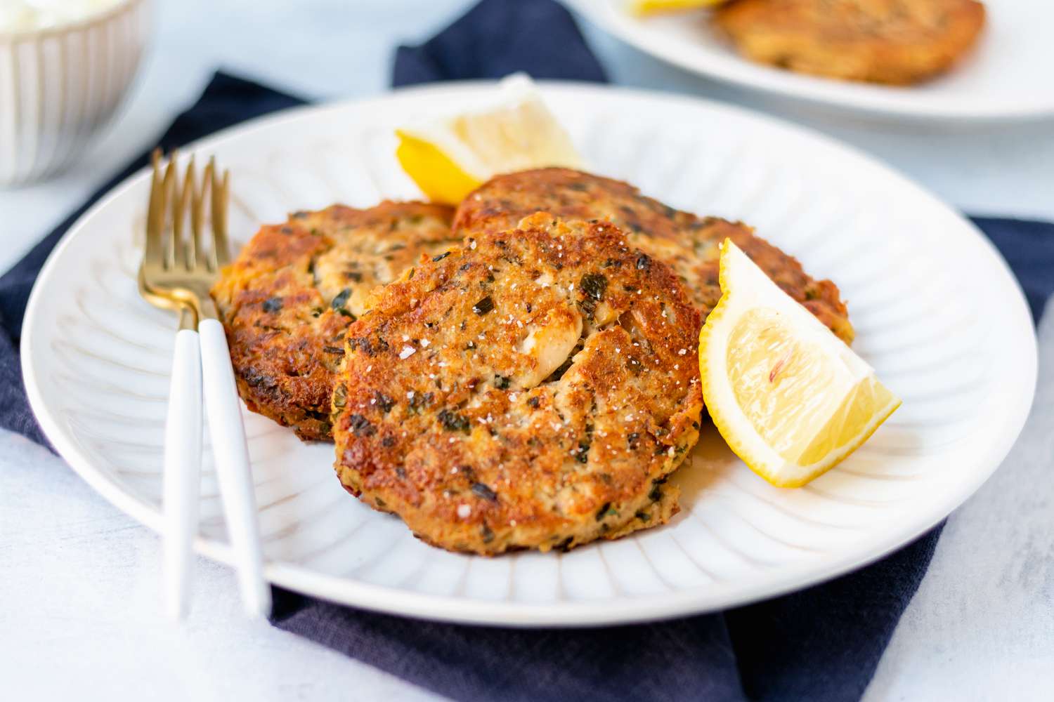 Tuna cakes on a white plate along with a lemon wedge and fork.