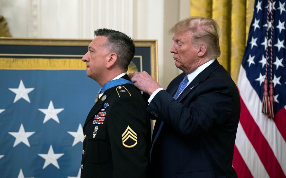 President Donald J. Trump puts a Medal of Honor on a blue ribbon around the neck of former U.S. Army Staff Sgt David G. Bellavia at the White House with an American flag in the background. 