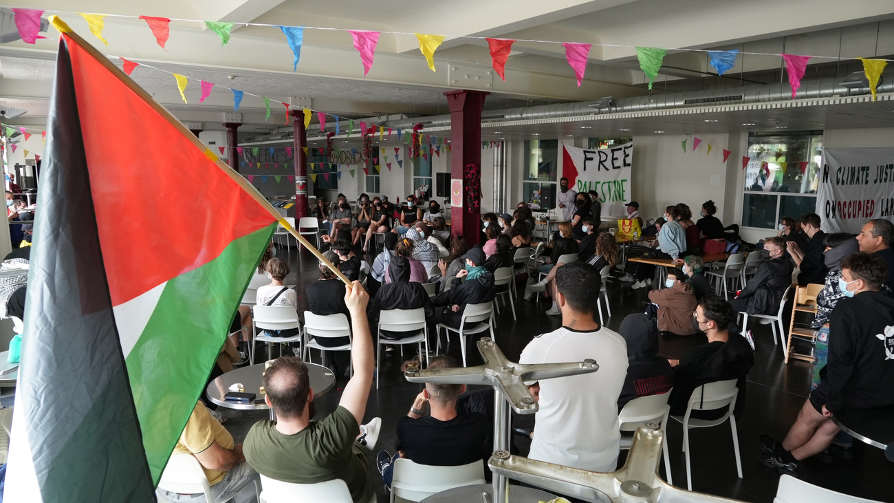 About 60 people crowd into the entrance of a university building. One is waving a Palestinian flag.