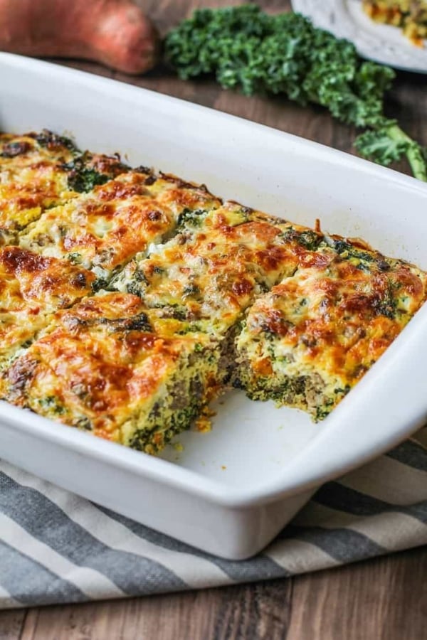 Sweet potato and sausage egg casserole in a baking dish with a piece missing, fresh out of the oven.