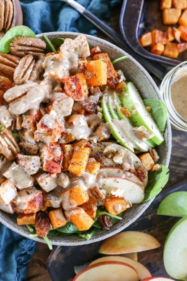 Top down close up image of a rustic bowl full of spinach salad with various ingredients like chicken, apples, pecans, and more.