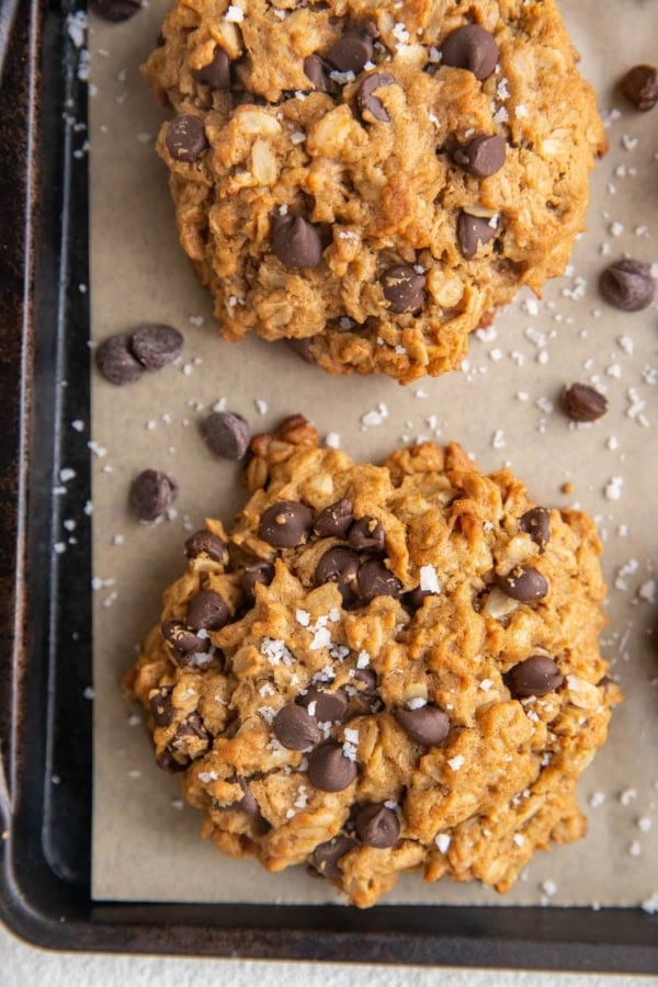 Baked peanut butter oatmeal cookies on a parchment lined baking sheet sprinkled with sea salt and extra chocolate chips.