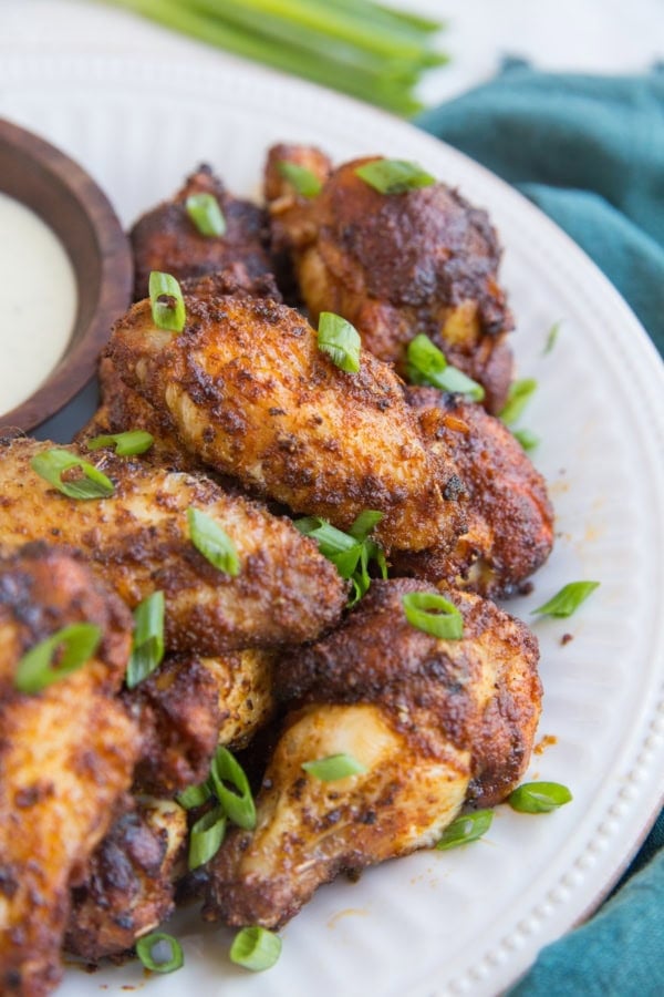 Big white plate with a pile of dry rub air fried chicken wings sprinkled with green onions with a dark blue napkin to the side.