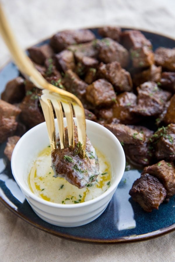 Blue plate full of air fryer steak bites with a small bowl of melted butter and a fork dipping a steak bite into the butter.