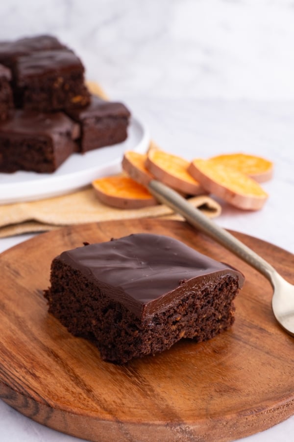 wooden plate with a slice of sweet potato chocolate cake on top with hunks of chocolate cake in the background.