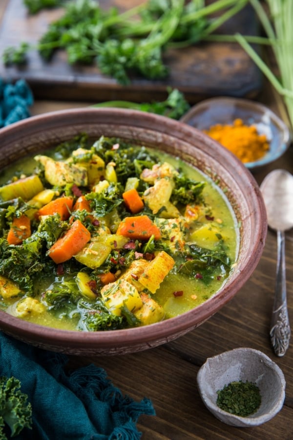 close up turmeric chicken soup in a brown bowl with a blue napkin to the side.