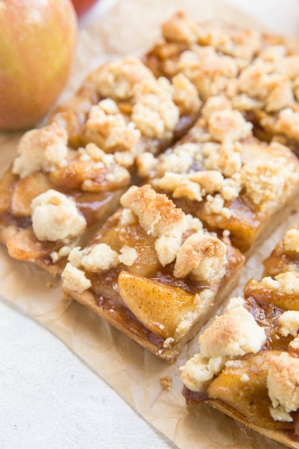 Sheet of parchment paper with gluten-free apple pie bars cut into slices. A fresh apple to the side.