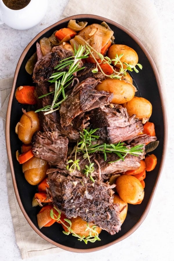 Platter of shredded beef on top of potatoes, carrots, and onions, ready to serve.